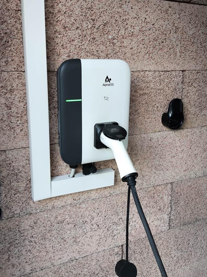 Wandmontierte Wallbox mit angestecktem Ladekabel an einer Hauswand, die Statusanzeige leuchtet grün